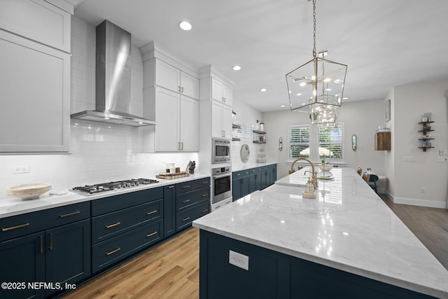 kitchen featuring white cabinetry, stainless steel appliances, an island with sink, and wall chimney range hood