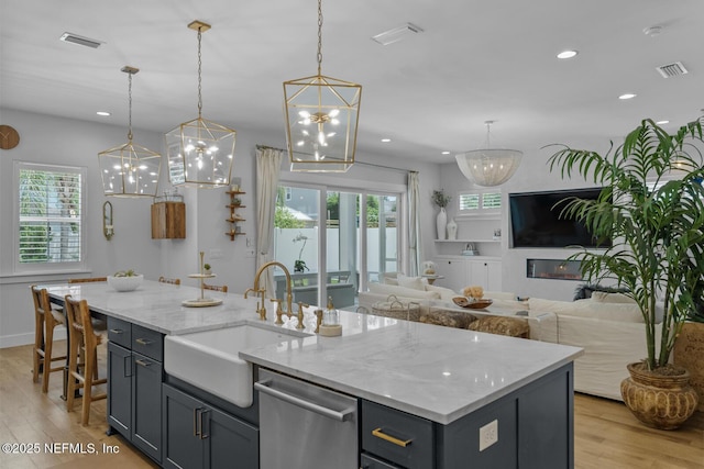 kitchen featuring pendant lighting, dishwasher, sink, an island with sink, and light hardwood / wood-style floors