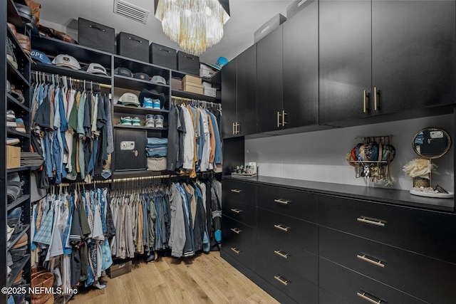 walk in closet featuring light hardwood / wood-style flooring and a notable chandelier