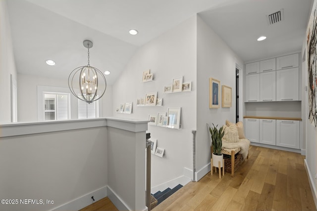 hallway featuring a notable chandelier, light wood-type flooring, and vaulted ceiling