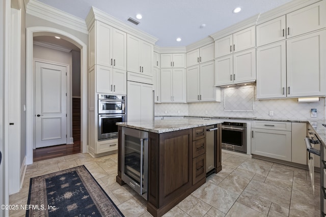 kitchen with wine cooler, light stone counters, double oven, crown molding, and decorative backsplash