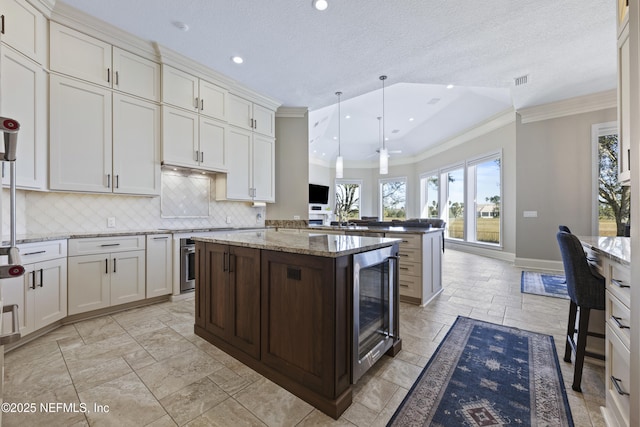 kitchen with light stone countertops, ceiling fan, a center island, wine cooler, and hanging light fixtures