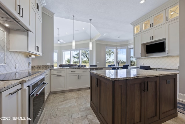 kitchen featuring kitchen peninsula, oven, decorative light fixtures, black electric cooktop, and ceiling fan with notable chandelier