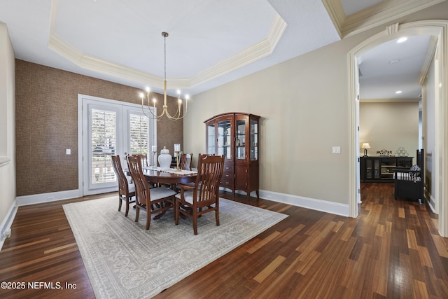 dining space with ornamental molding, dark hardwood / wood-style flooring, a tray ceiling, and a notable chandelier