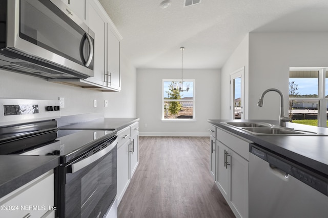 kitchen with appliances with stainless steel finishes, decorative light fixtures, sink, white cabinets, and dark wood-type flooring