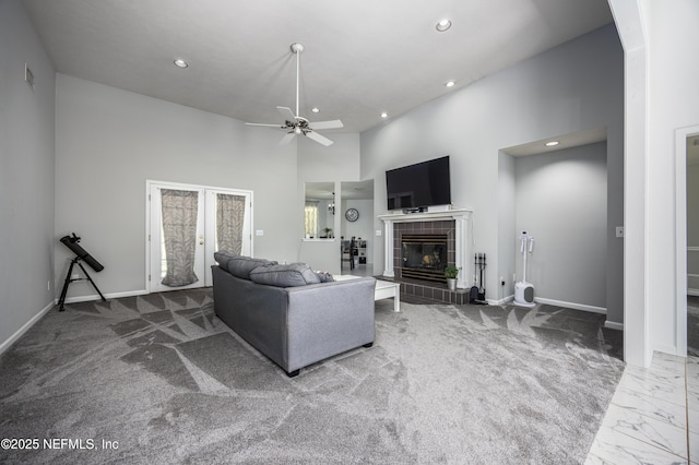 carpeted living room featuring a tiled fireplace, ceiling fan, french doors, and a high ceiling