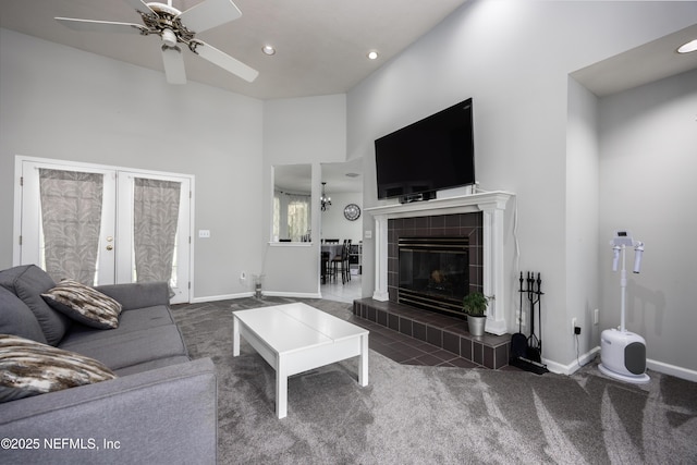 living room featuring dark carpet, a high ceiling, french doors, ceiling fan, and a tiled fireplace