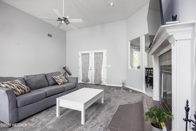 carpeted living room featuring ceiling fan, a high ceiling, and a tiled fireplace