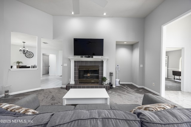 carpeted living room featuring ceiling fan with notable chandelier, a towering ceiling, and a tile fireplace