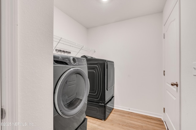 laundry area with washing machine and clothes dryer and light hardwood / wood-style floors