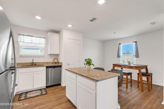 kitchen featuring sink, appliances with stainless steel finishes, a kitchen island, light stone countertops, and white cabinets