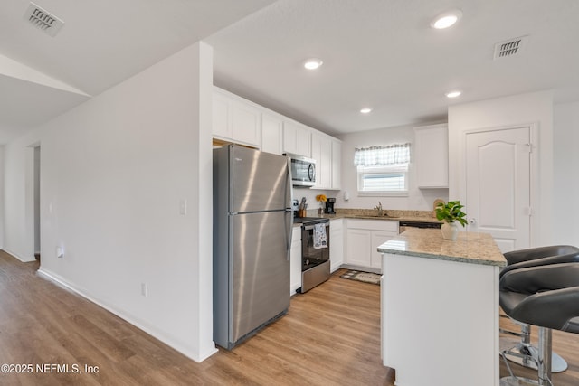 kitchen with white cabinetry, sink, a kitchen bar, stainless steel appliances, and light wood-type flooring