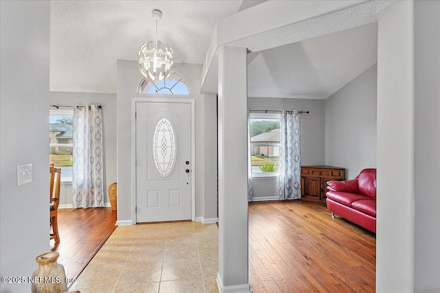 entrance foyer featuring light hardwood / wood-style flooring, an inviting chandelier, vaulted ceiling, and plenty of natural light