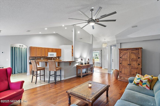 living room featuring light hardwood / wood-style floors, ceiling fan with notable chandelier, vaulted ceiling, and a textured ceiling