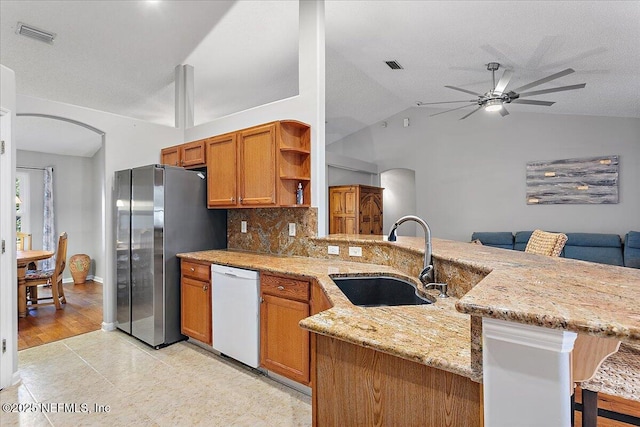 kitchen with dishwasher, vaulted ceiling, kitchen peninsula, stainless steel fridge, and sink