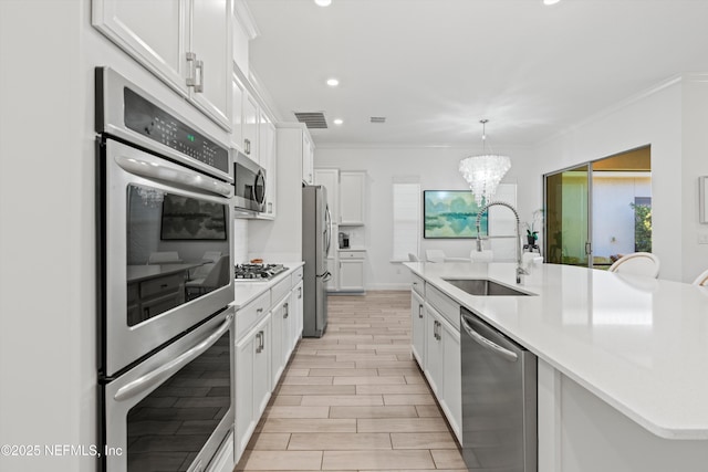 kitchen featuring white cabinets, a center island with sink, stainless steel appliances, pendant lighting, and sink