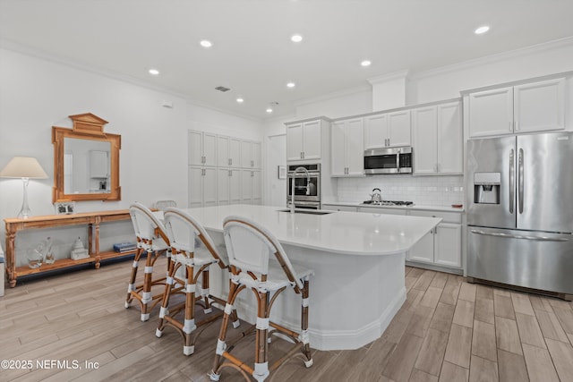 kitchen with a center island with sink, white cabinets, crown molding, and appliances with stainless steel finishes