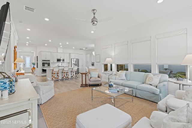 living room with ornamental molding, ceiling fan, and light hardwood / wood-style floors