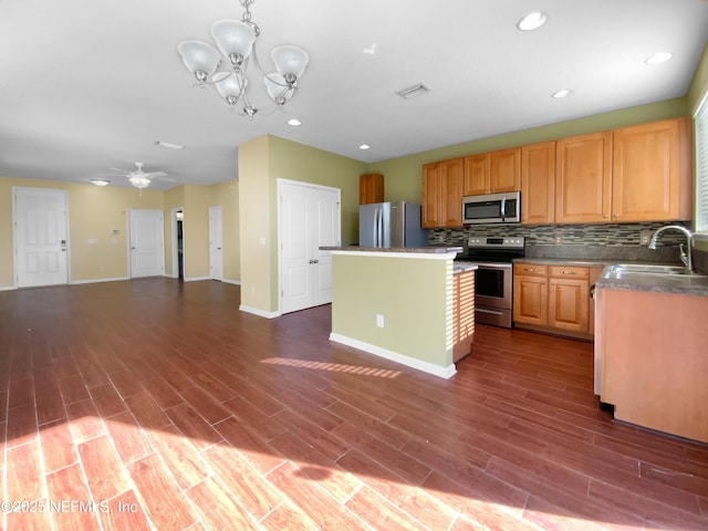 kitchen with tasteful backsplash, ceiling fan with notable chandelier, stainless steel appliances, sink, and a center island