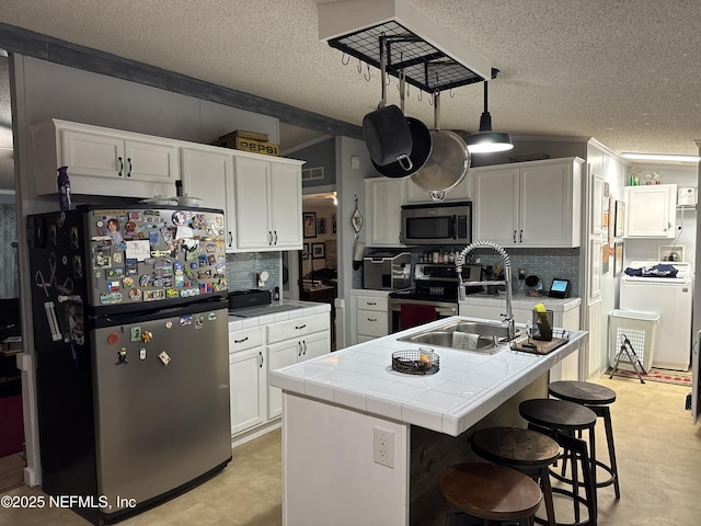 kitchen featuring tasteful backsplash, stainless steel appliances, white cabinetry, tile counters, and an island with sink