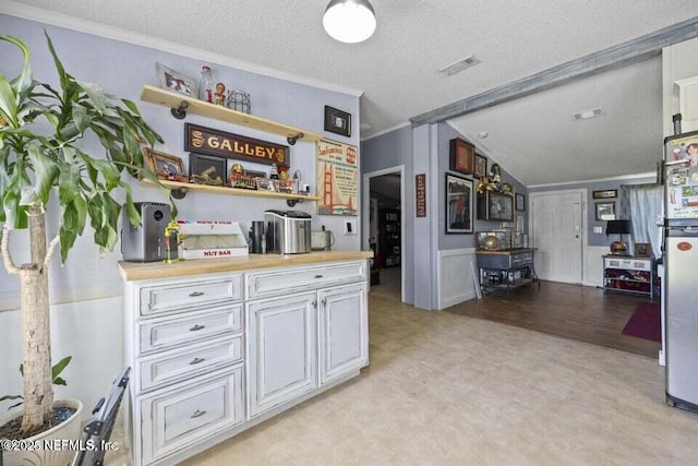 kitchen with stainless steel fridge, a textured ceiling, white cabinetry, and ornamental molding