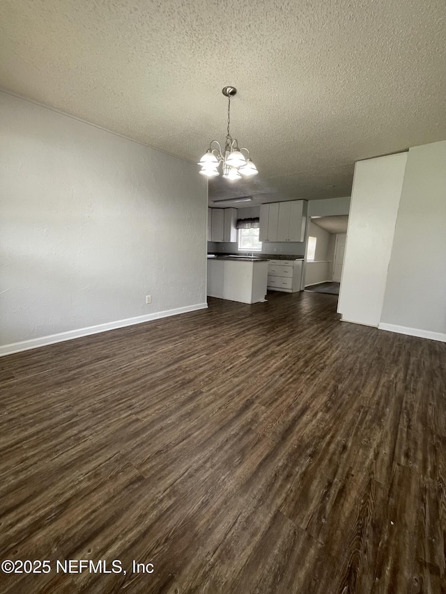 unfurnished living room featuring dark wood-type flooring, a textured ceiling, and an inviting chandelier