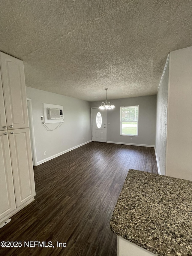 interior space featuring a wall mounted air conditioner, a notable chandelier, dark wood-type flooring, and a textured ceiling