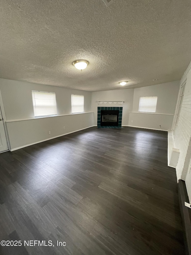 unfurnished living room featuring dark hardwood / wood-style floors, a textured ceiling, and a tiled fireplace