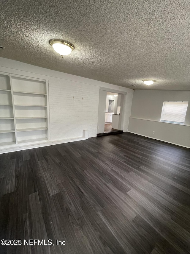 empty room with a textured ceiling, built in shelves, and dark hardwood / wood-style floors