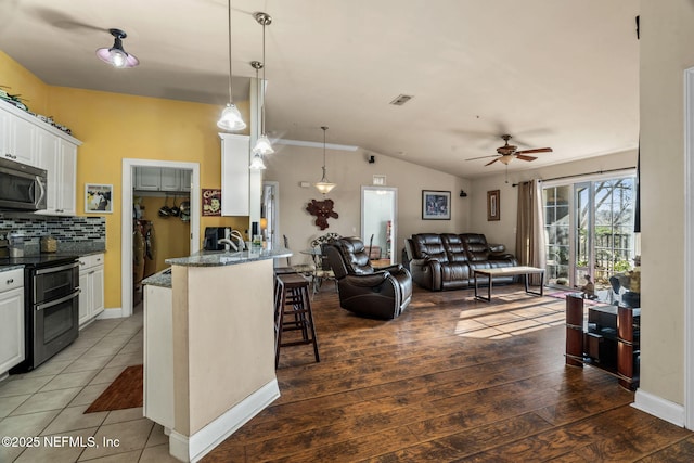 kitchen with a breakfast bar, white cabinetry, dark stone countertops, hanging light fixtures, and stainless steel appliances