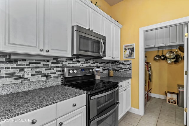 kitchen featuring tasteful backsplash, dark stone countertops, white cabinets, light tile patterned floors, and stainless steel appliances