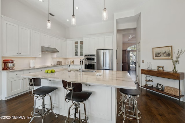 kitchen with stainless steel appliances, white cabinetry, hanging light fixtures, and a kitchen island with sink