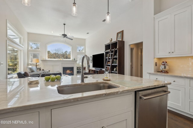 kitchen featuring pendant lighting, stainless steel dishwasher, sink, and light stone counters