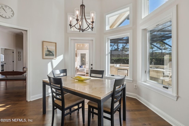 dining space with dark wood-type flooring, a towering ceiling, a chandelier, and a wealth of natural light