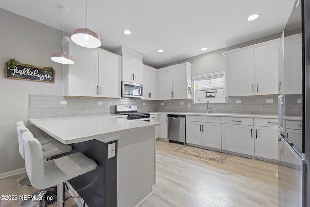 kitchen with kitchen peninsula, white cabinets, decorative light fixtures, and appliances with stainless steel finishes