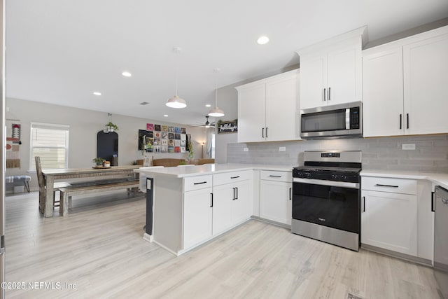 kitchen with kitchen peninsula, pendant lighting, stainless steel appliances, and white cabinetry