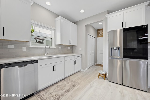 kitchen with appliances with stainless steel finishes, tasteful backsplash, sink, light hardwood / wood-style flooring, and white cabinetry