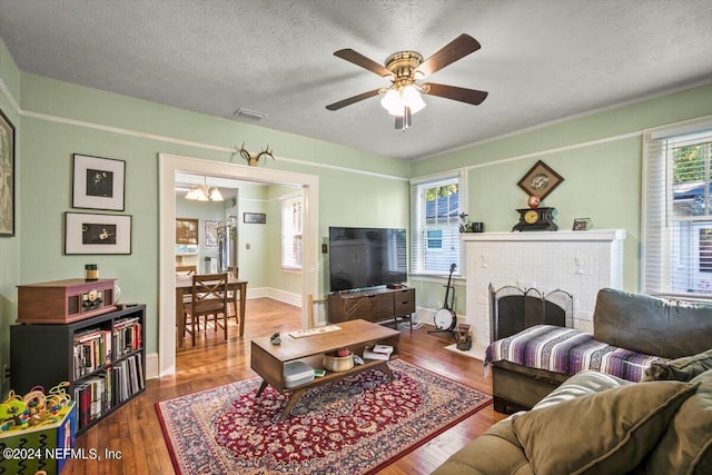 living room with ceiling fan, a fireplace, hardwood / wood-style floors, and a textured ceiling