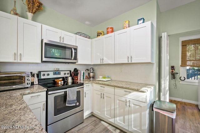 kitchen featuring light stone countertops, light wood-type flooring, backsplash, stainless steel appliances, and white cabinetry