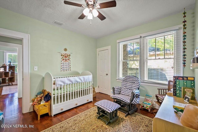 bedroom featuring a textured ceiling, ceiling fan, a crib, and dark wood-type flooring