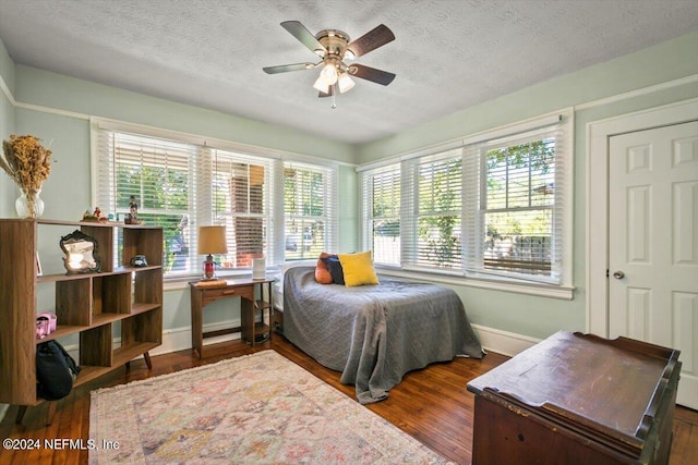 bedroom featuring a textured ceiling, ceiling fan, dark wood-type flooring, and multiple windows