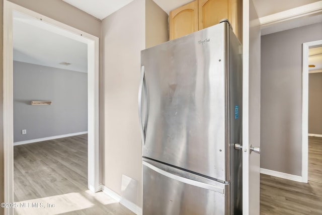 kitchen featuring light wood-style flooring, light brown cabinets, freestanding refrigerator, and baseboards