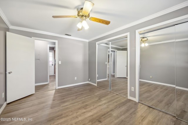 unfurnished bedroom with wood finished floors, visible vents, baseboards, multiple closets, and ornamental molding