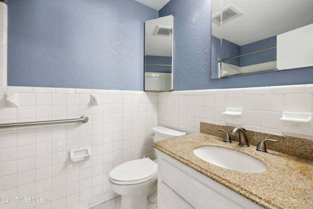 bathroom with a textured wall, vanity, visible vents, and tile walls