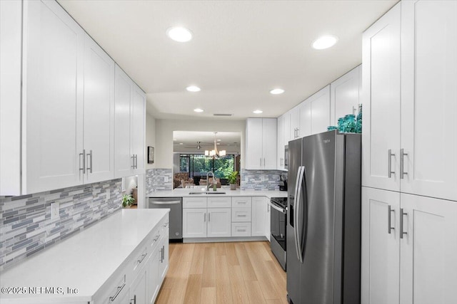 kitchen with sink, light hardwood / wood-style flooring, appliances with stainless steel finishes, a notable chandelier, and white cabinetry