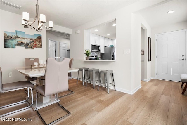 dining space featuring light wood-type flooring and an inviting chandelier