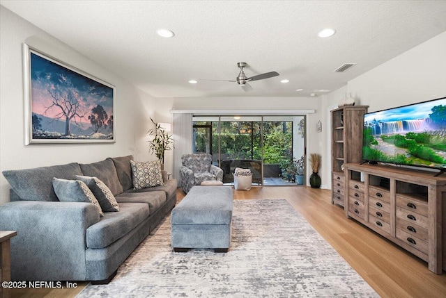 living room featuring ceiling fan, light wood-type flooring, and a textured ceiling