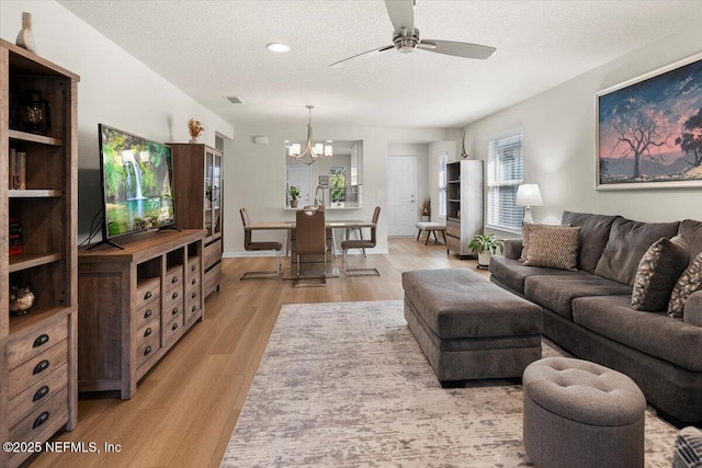 living room featuring ceiling fan with notable chandelier, light hardwood / wood-style floors, and a textured ceiling