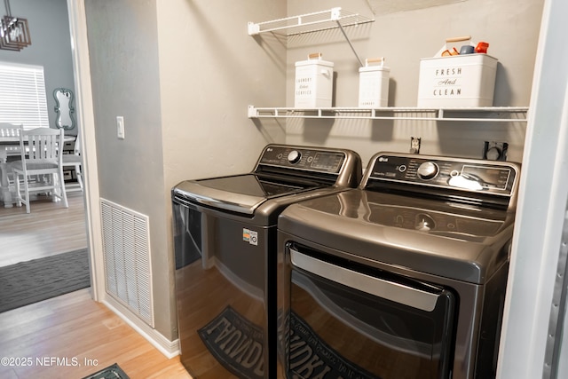 clothes washing area with washing machine and dryer and light hardwood / wood-style floors