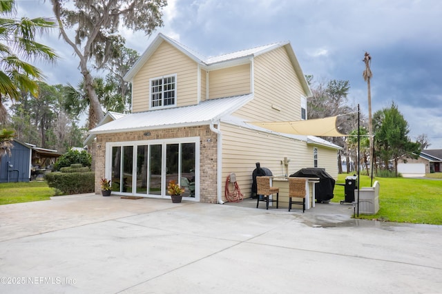 back of house with concrete driveway, a patio, metal roof, a yard, and brick siding